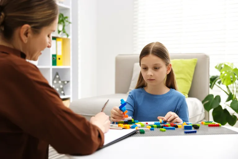 Child engaged in play therapy with colorful building blocks and a therapist