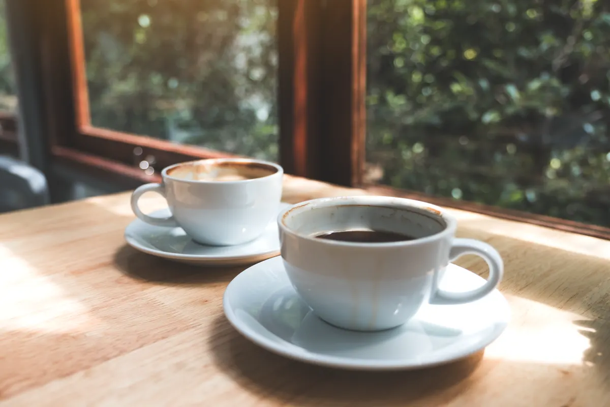 Two coffee cups on a wooden table in warm window light